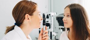 Doctor Optometrist examining teenage girl's eye in doctors office